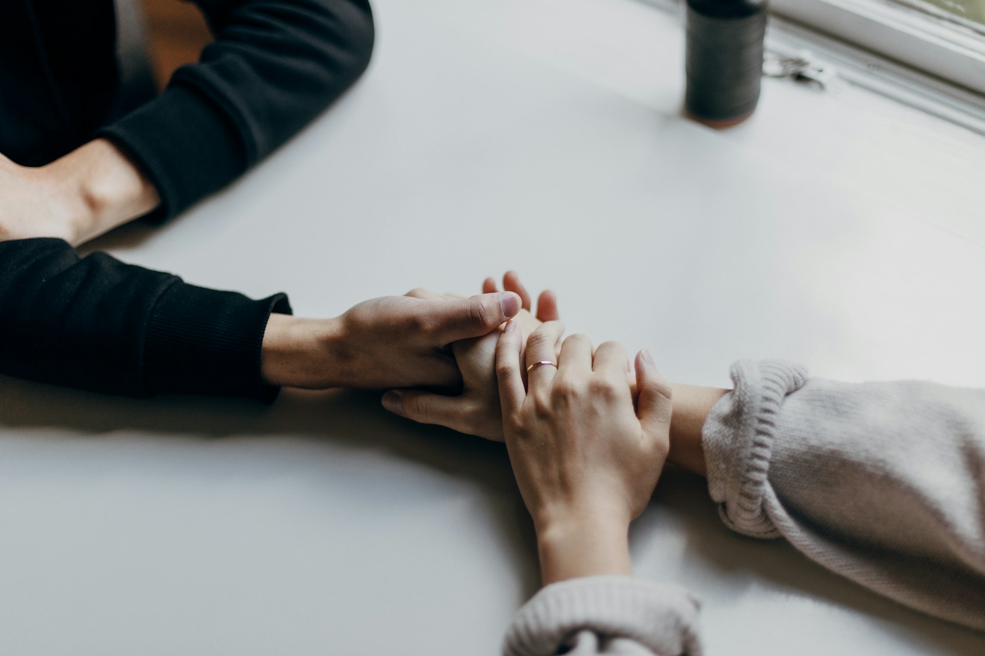 Two people holding hands across a table in a moment of support