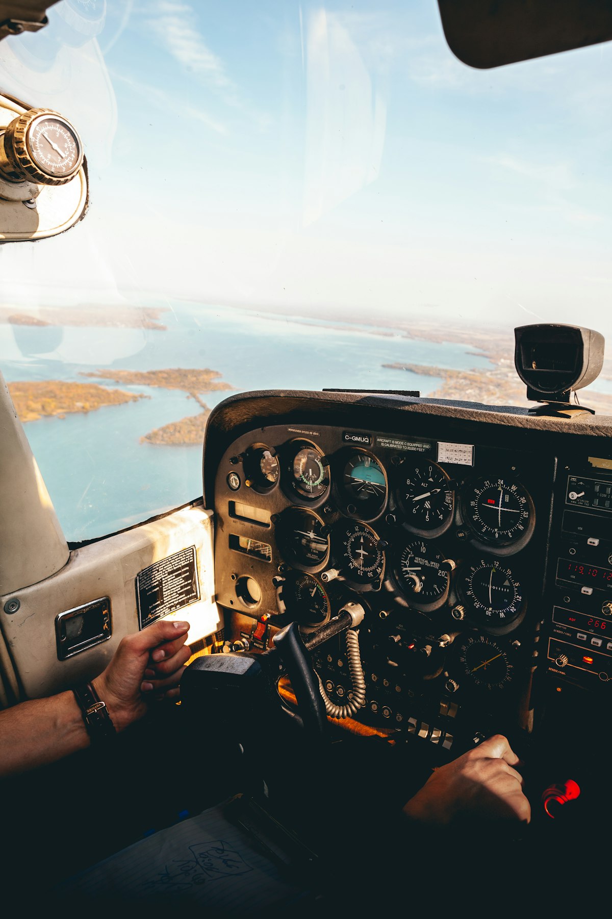 A pilot's hands on the controls in a small aircraft cockpit, a bay of islands ahead