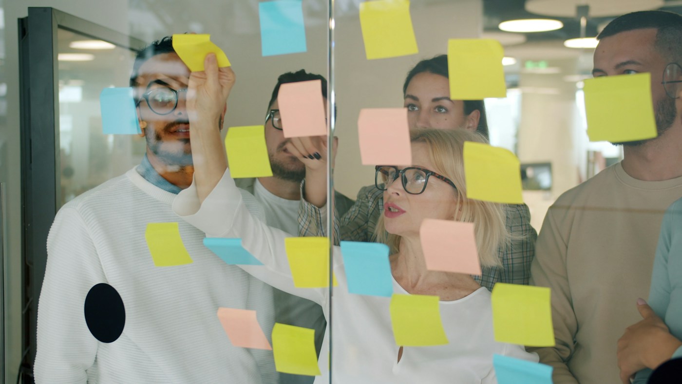 A team working through a problem together with sticky notes on a glass wall