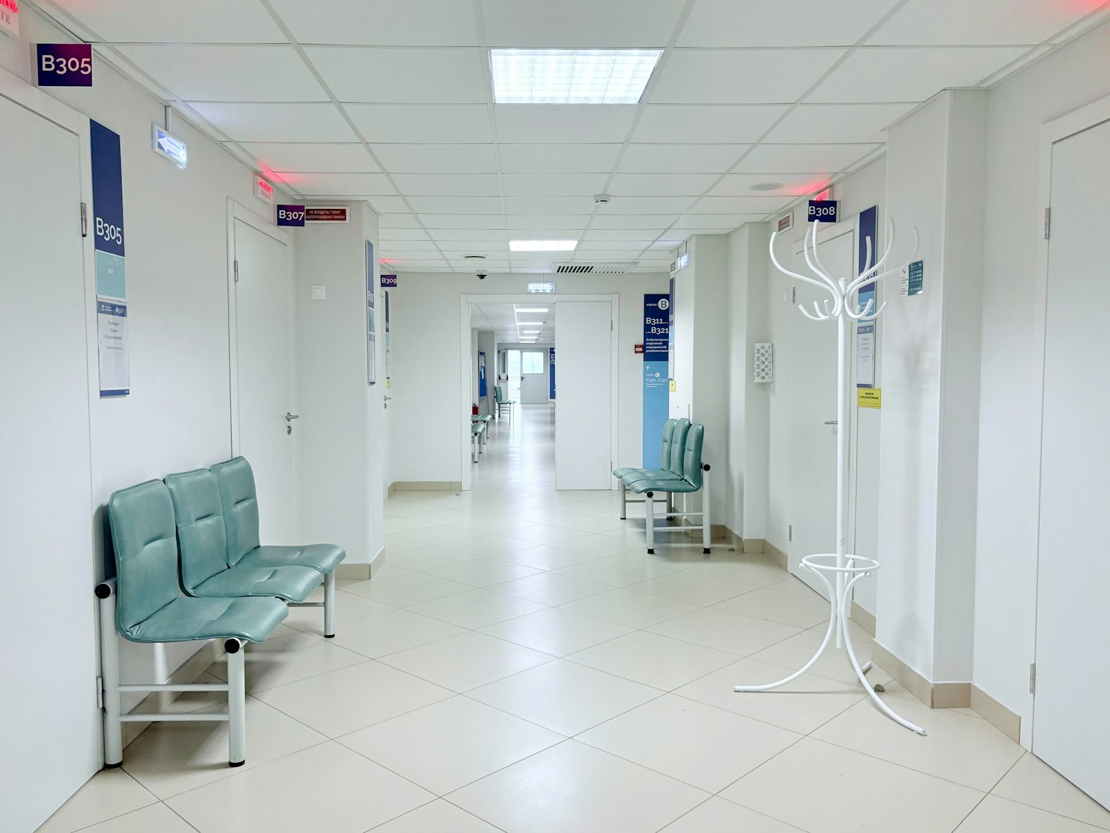 A long, bright hospital corridor with benches and doors