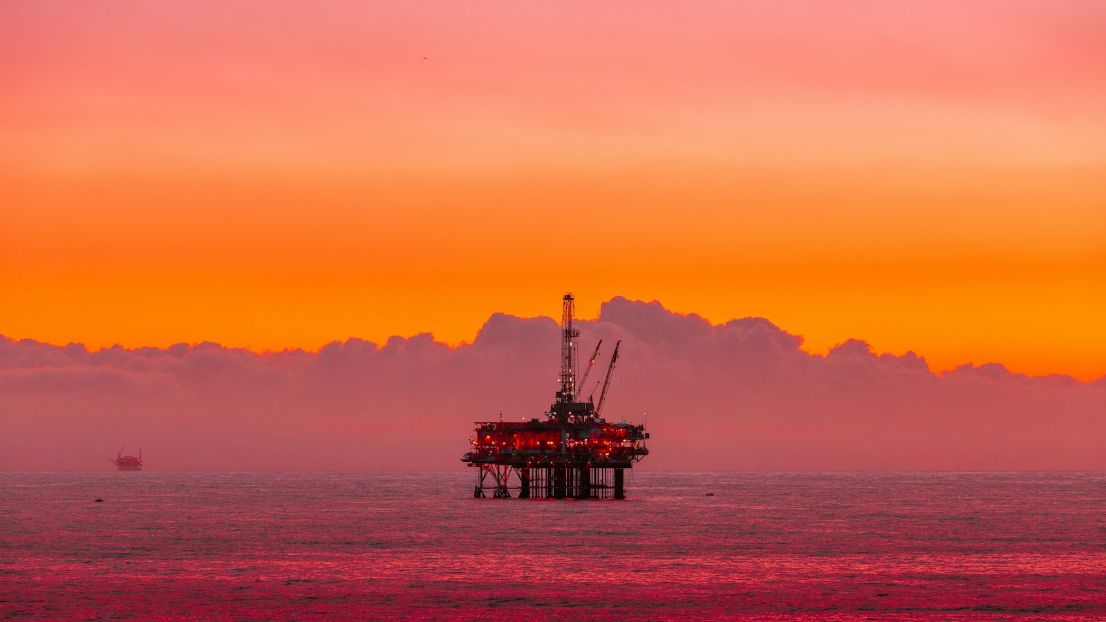 An offshore oil rig standing in the sea under an orange sunset