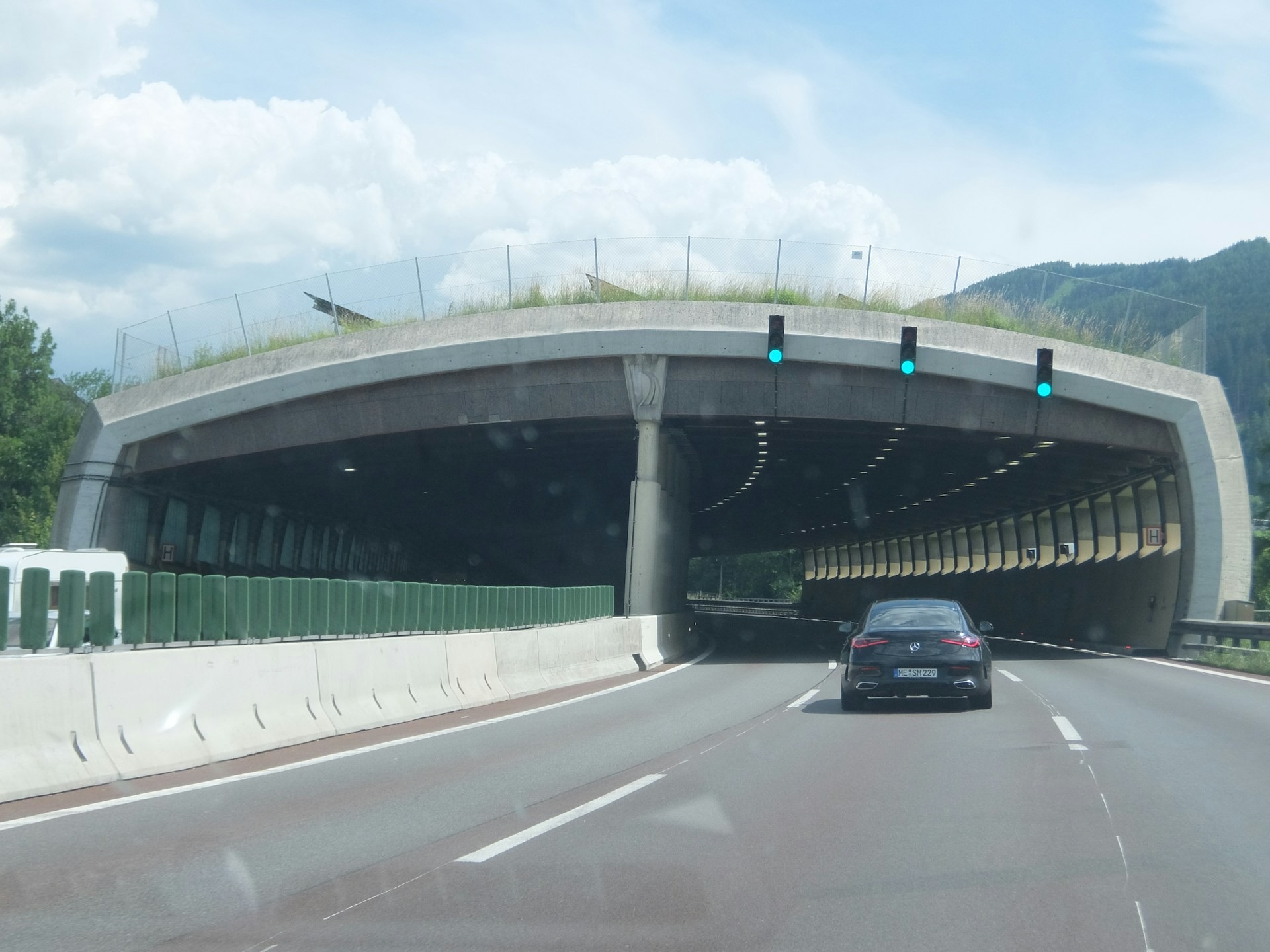 A car approaching a modern highway tunnel with green lights