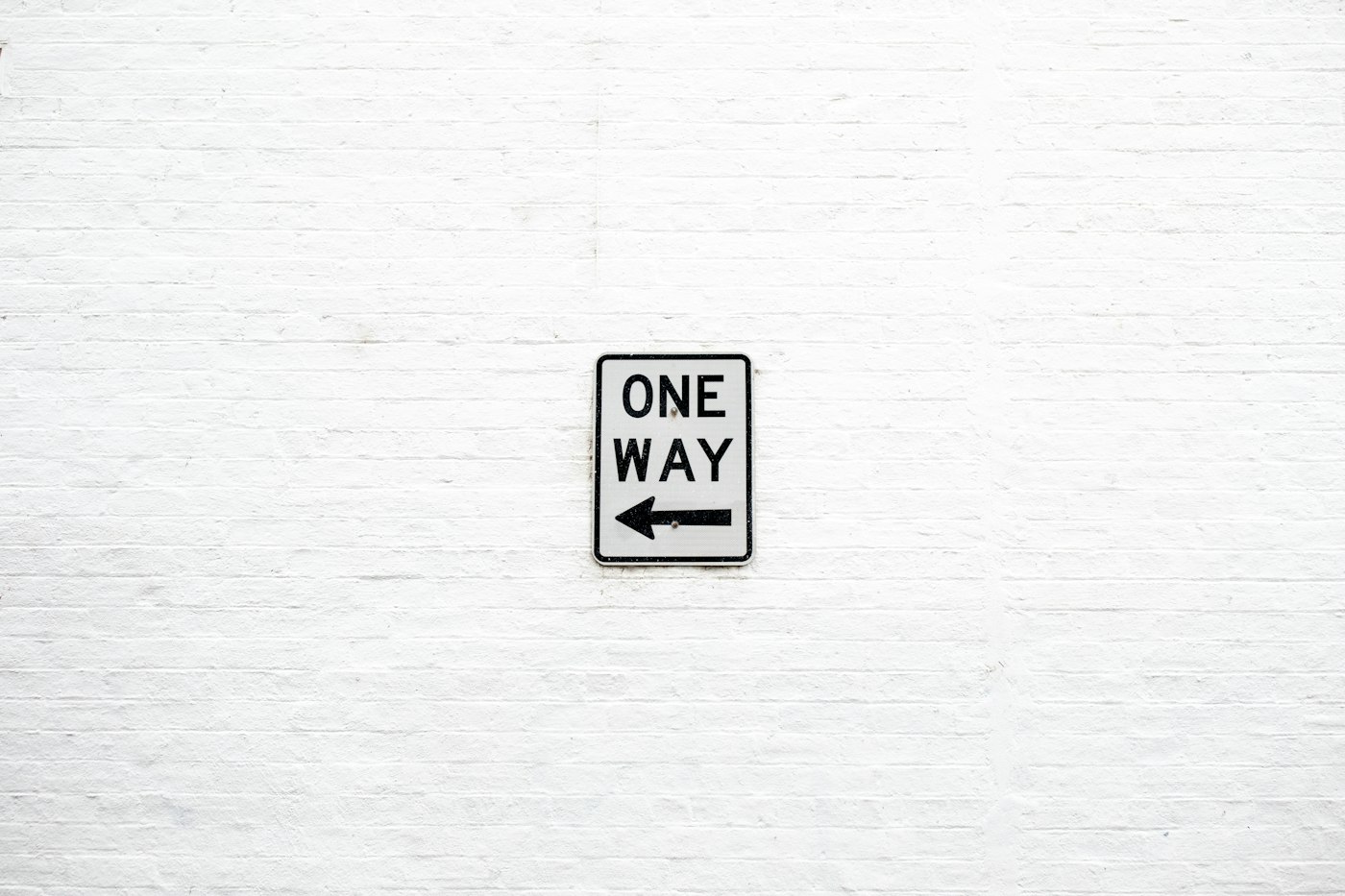 A single One Way sign on a plain white wall