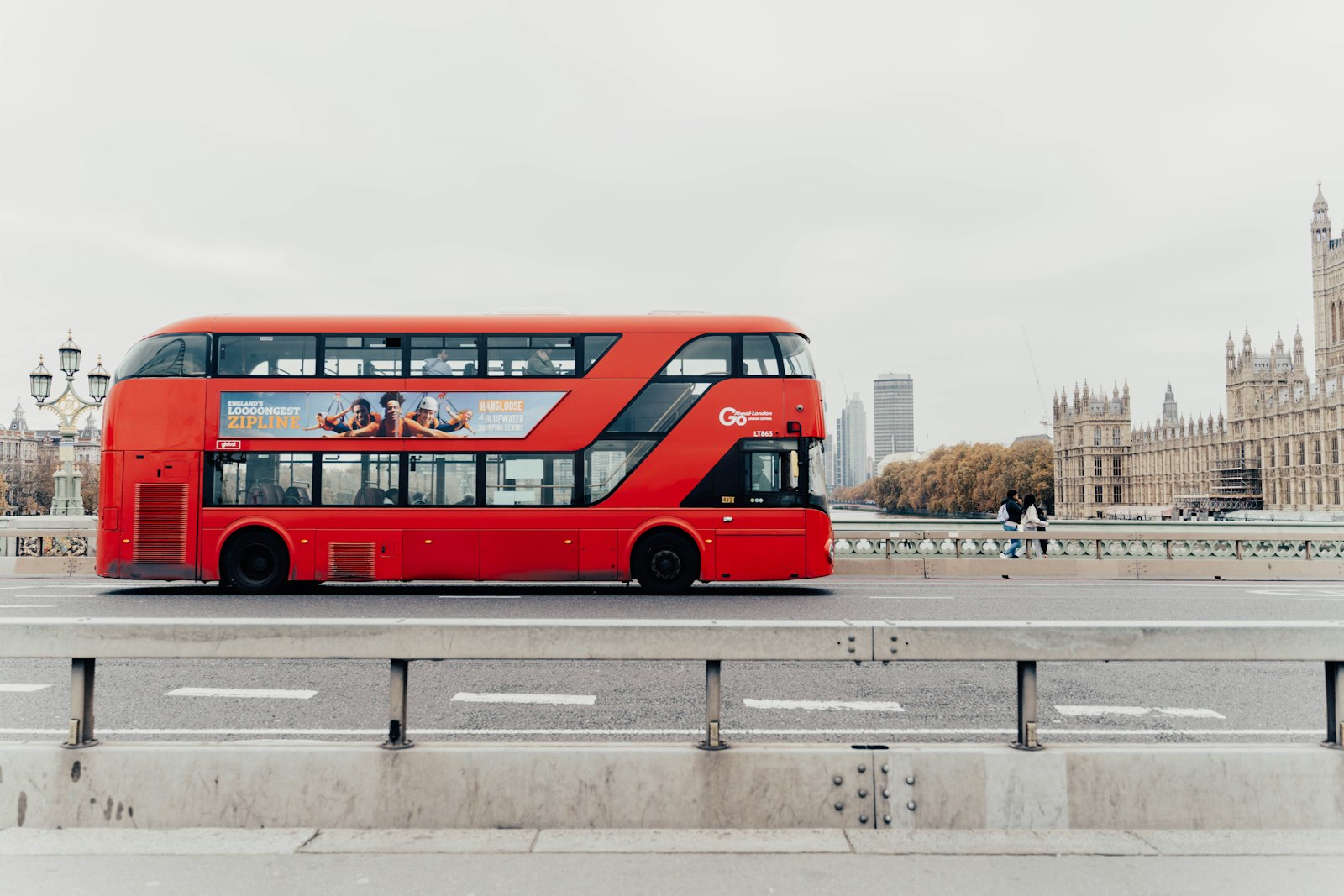 A red double-decker bus crossing a bridge, with the Houses of Parliament behind